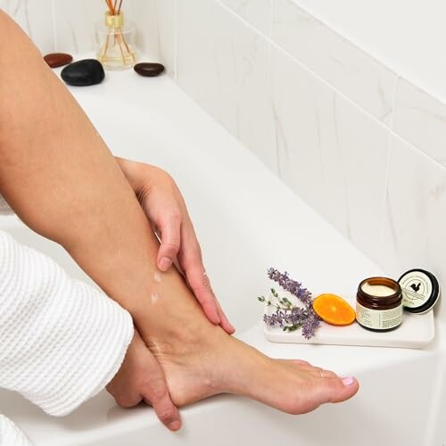 Person applying lotion on leg beside skincare products in a bathroom.